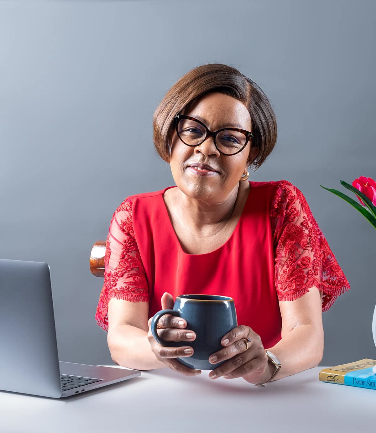 Ann W. Muraya seated at a desk, holding a mug.